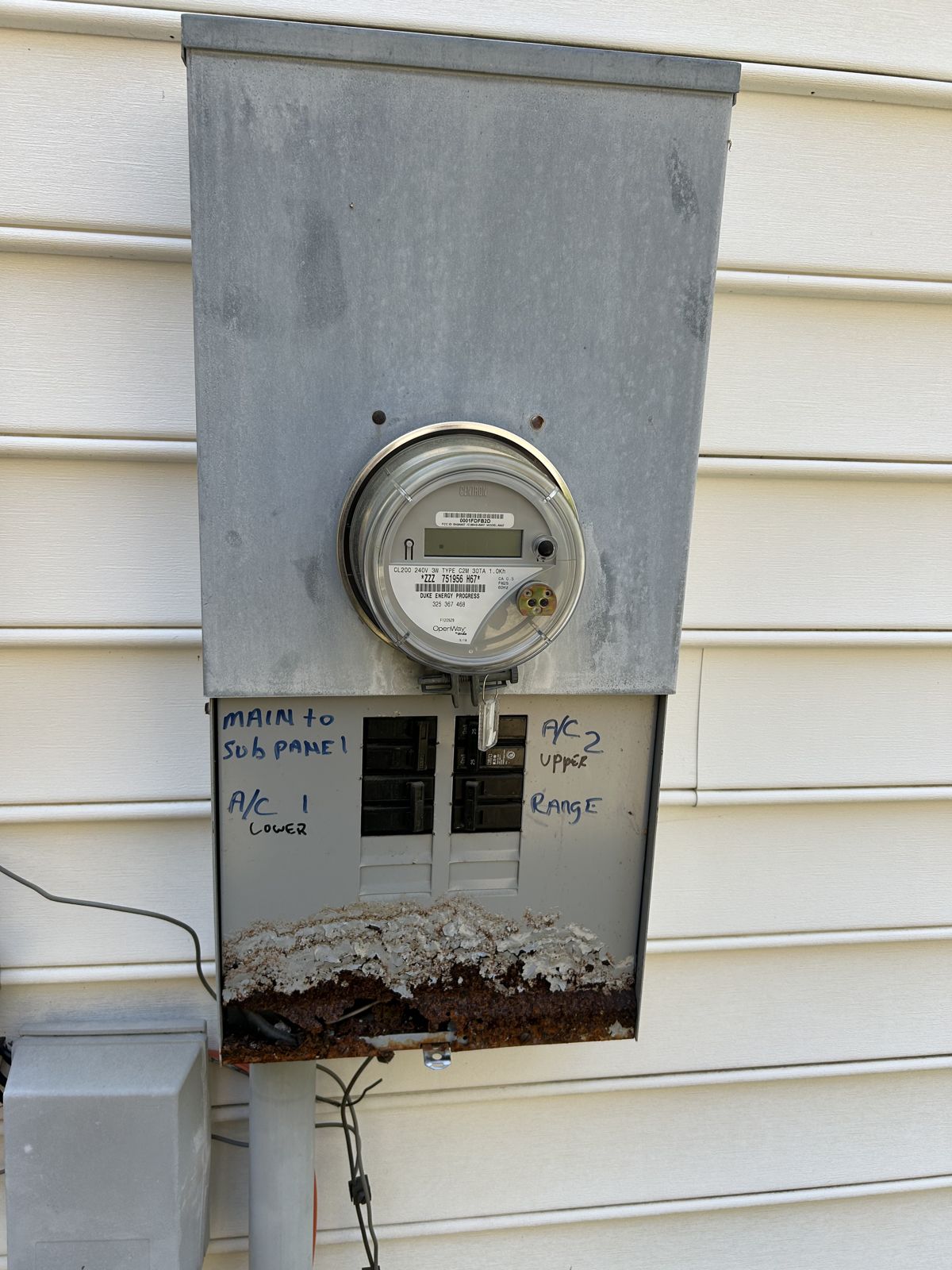 Old meter combo with its breaker cover open, showing heavy rust along the bottom of the enclosure