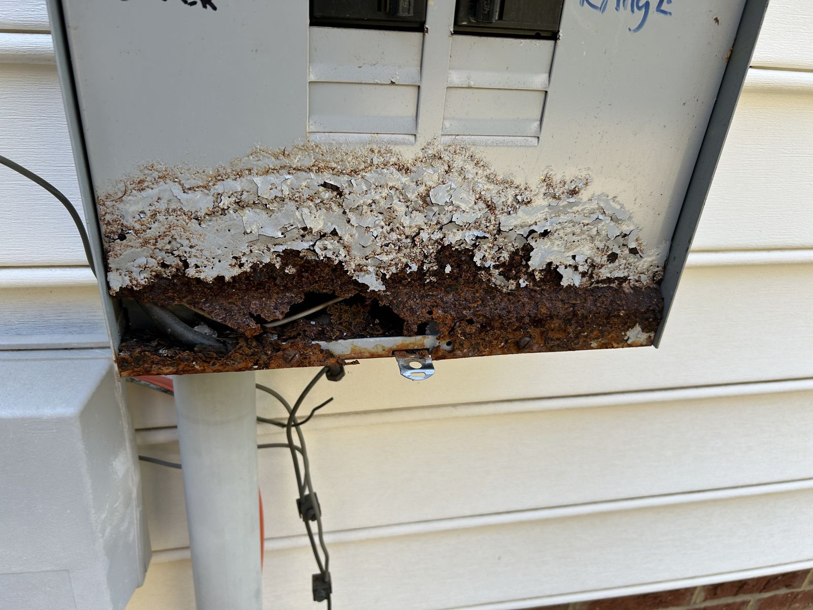 Close-up of the rusted-through bottom of an outdoor electrical meter combo enclosure