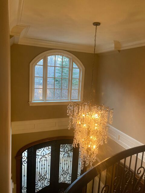Cascading crystal chandelier hung in a two-story foyer above an arched iron front door