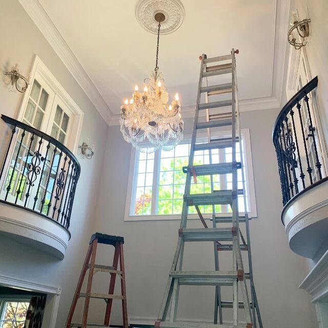 Crystal chandelier being installed in a two-story foyer from ladders between the balconies