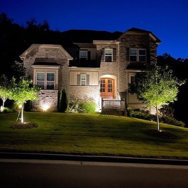 Landscape uplighting on a stone home and the trees in front of it