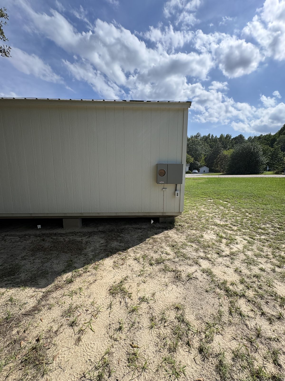 Detached shed with a new meter combo mounted on its side wall, seen across the yard